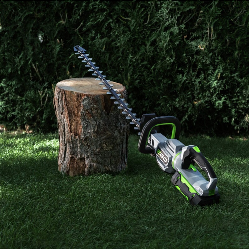 A green/black/gray hedge trimmer leaned on a block of wood